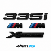 Gloss black BMW 335i rear lettering, xDrive plaque and two M wing badges with blue and red stripes.